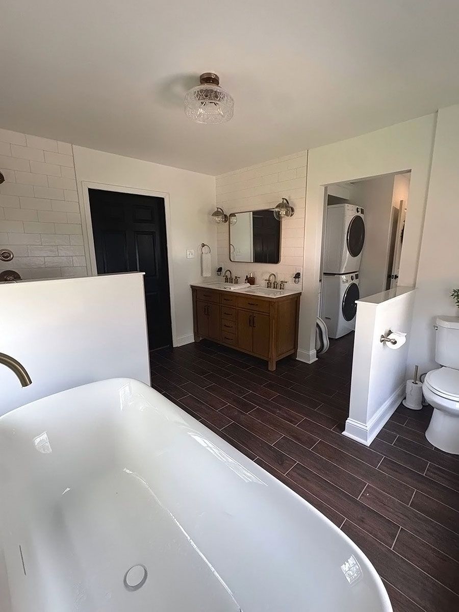 Bathroom interior with white tub, dark floor, wood vanity, and black door.