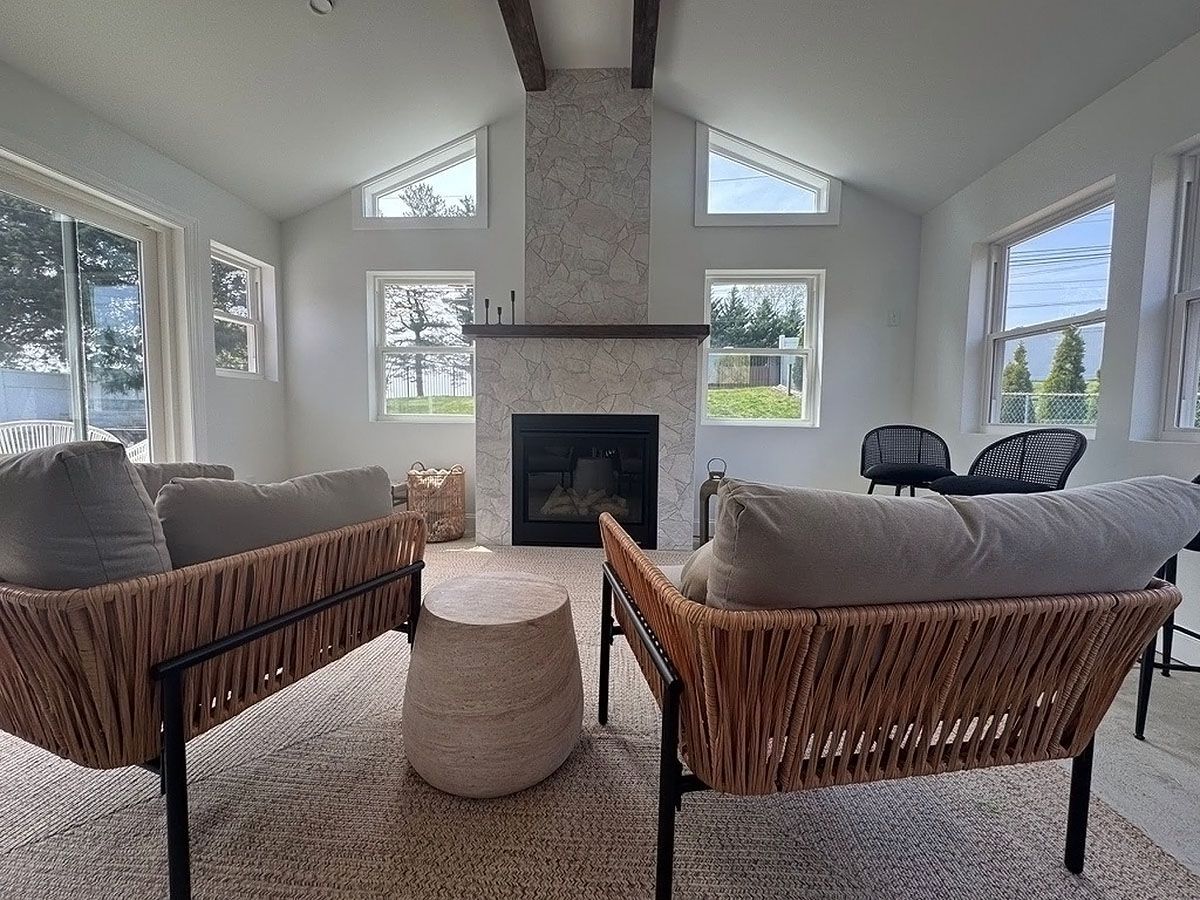 Bright living room with wicker chairs, fireplace, and large windows overlooking water