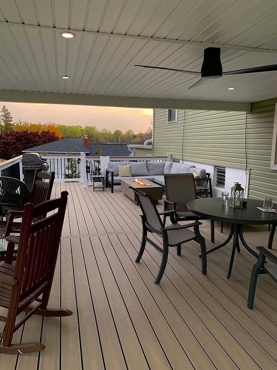 Covered deck with outdoor tables and chairs, white siding, and a sunset view beyond the railing
