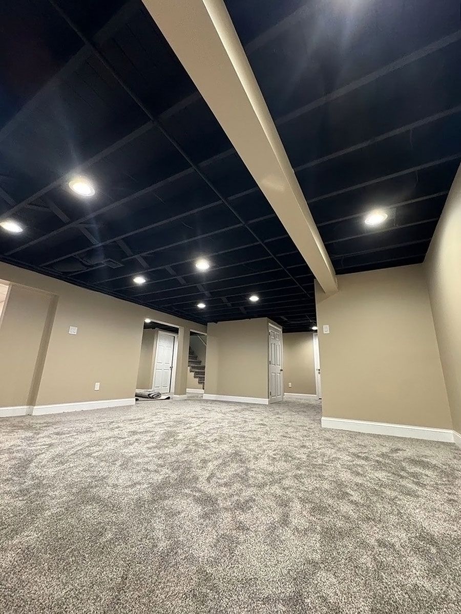 Empty carpeted room with beige walls, black ceiling, and recessed lights.
