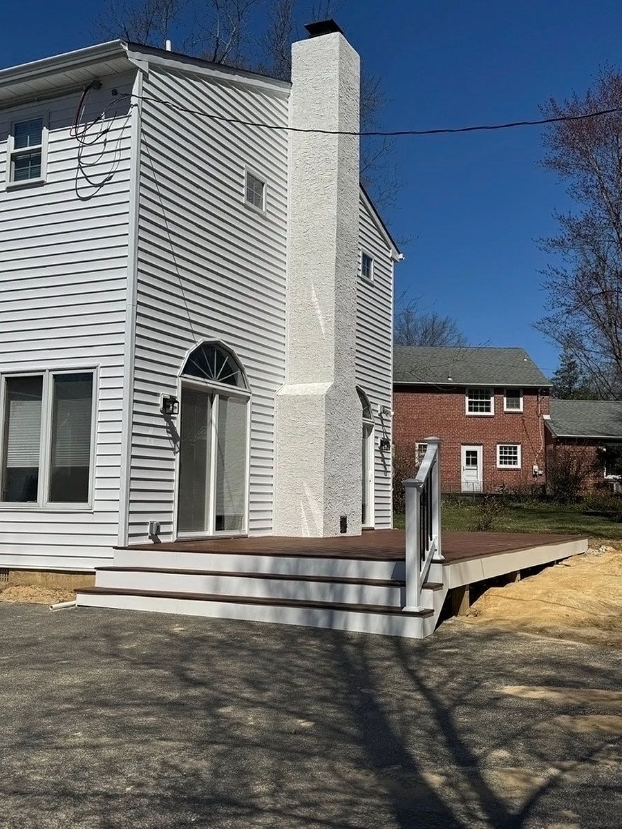 White house exterior with arched door, steps, and a brick house in the background under a clear blue sky