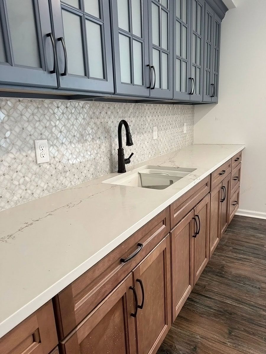 Kitchen countertop with white sink, black faucet, blue upper cabinets, and wood lower cabinets.