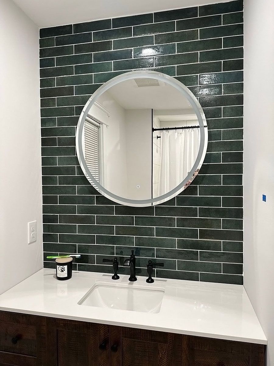 Bathroom vanity with round mirror, black tile backsplash, and white countertop sink