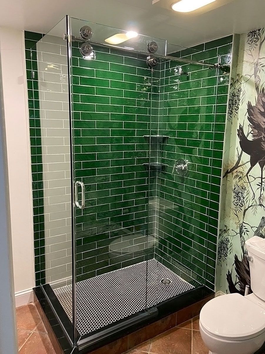 Green tiled glass shower with black base and patterned floor in a bathroom, beside a white toilet