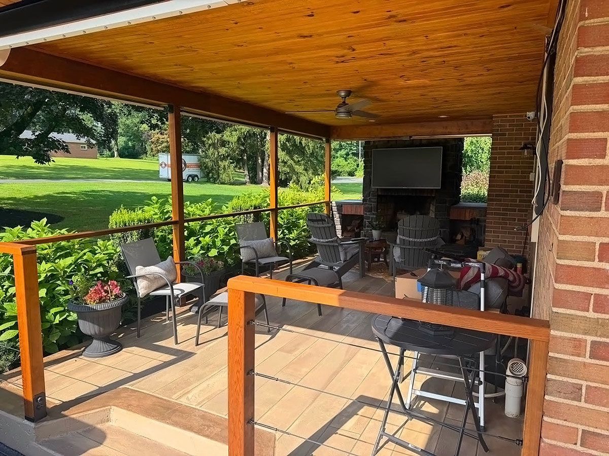 Covered patio with outdoor seating, brick walls, TV, and a view of a green lawn and trees.