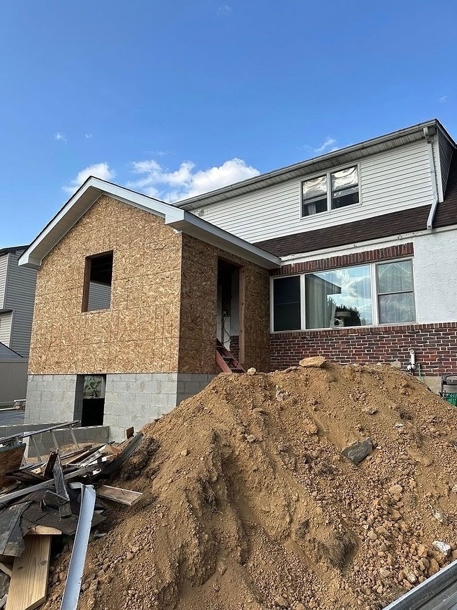 Partially built house with siding, windows, and large dirt piles in front under a clear blue sky