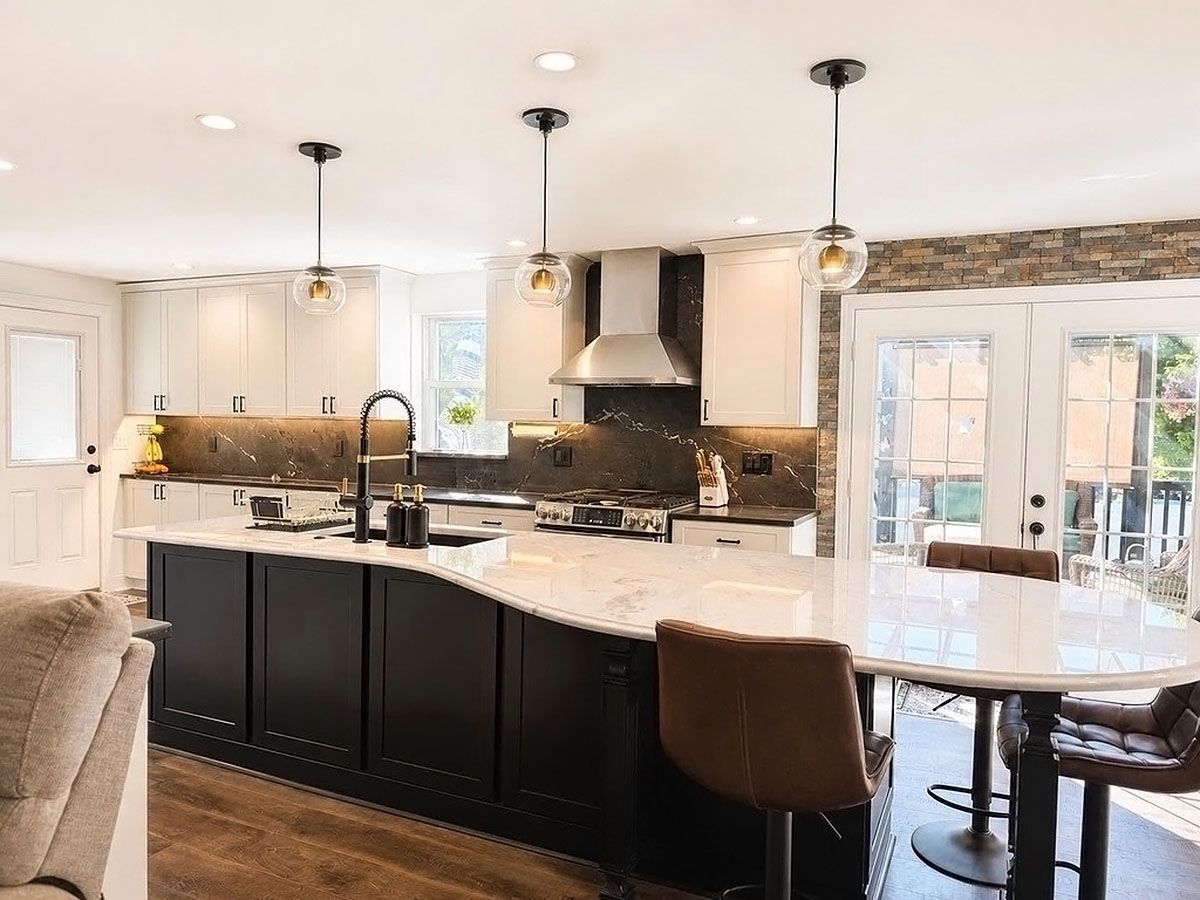 Bright modern kitchen with white cabinets, dark island, marble countertop, and pendant lights