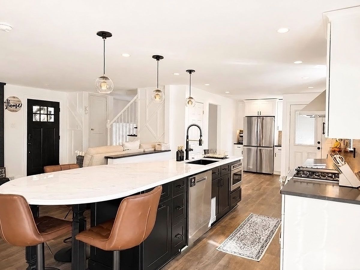 Bright modern kitchen with white cabinets, curved island, pendant lights, and stainless steel appliances