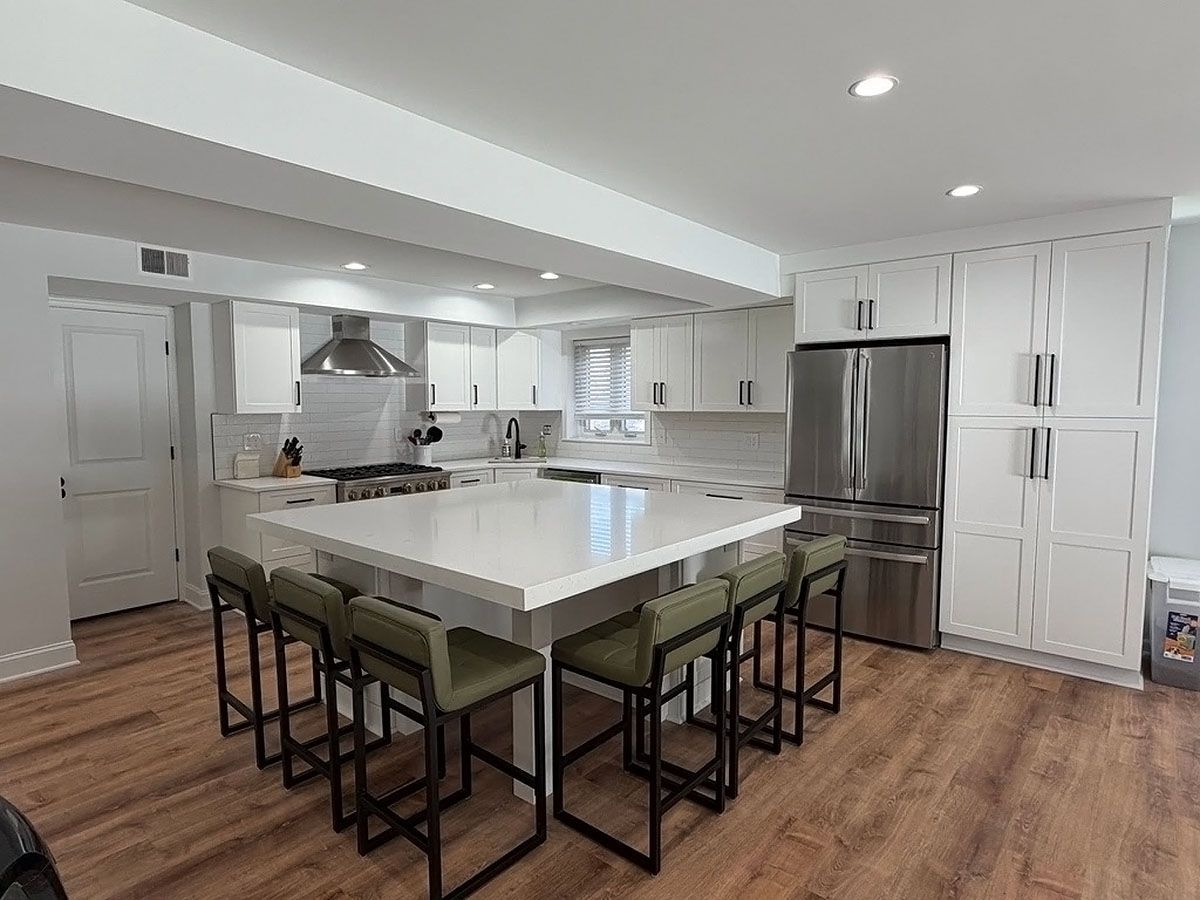 Modern white kitchen with large island, bar stools, stainless steel fridge, and wood floors