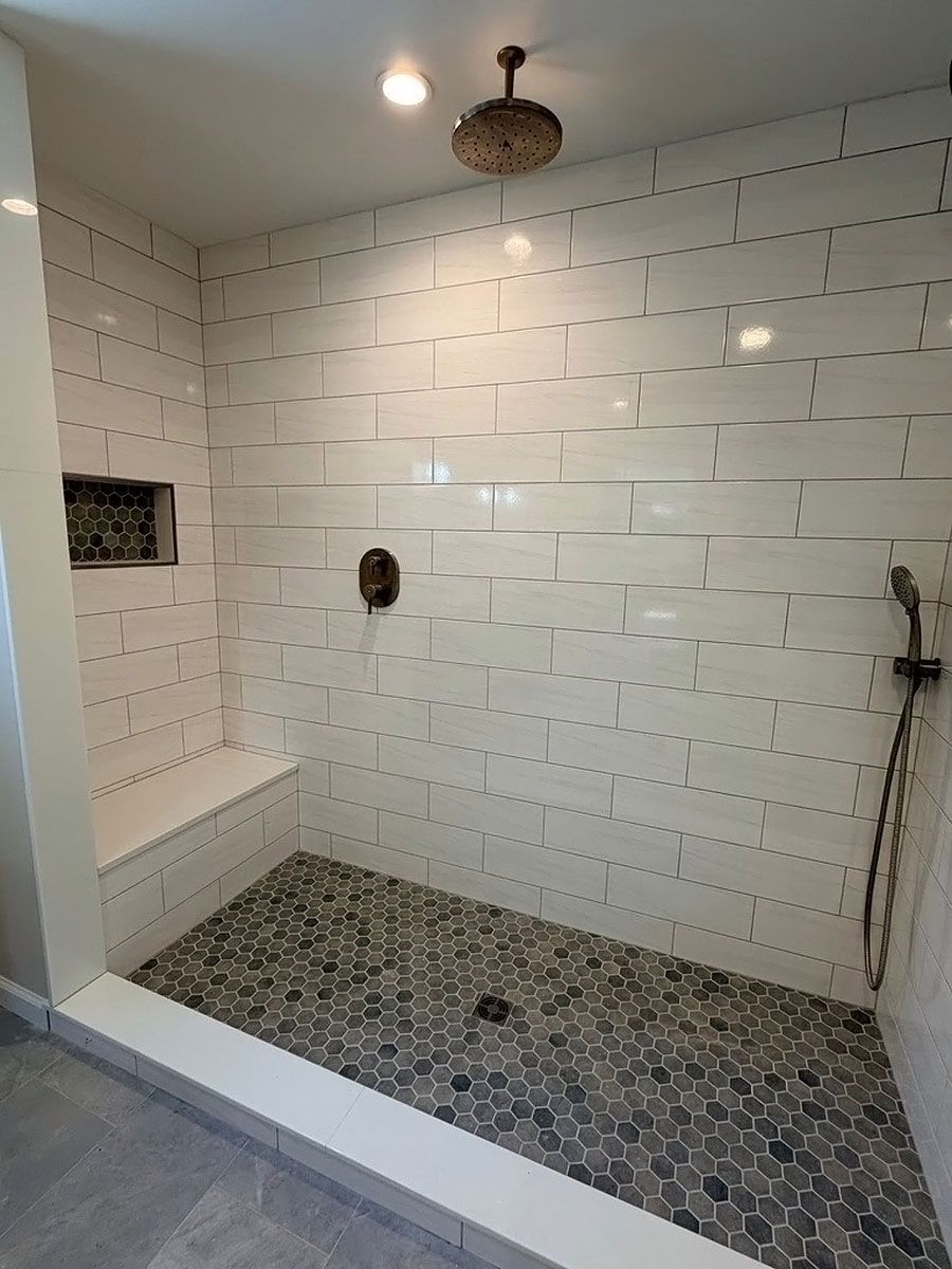 Walk-in shower with white subway tile, pebble floor, built-in bench, and showerhead on the right.