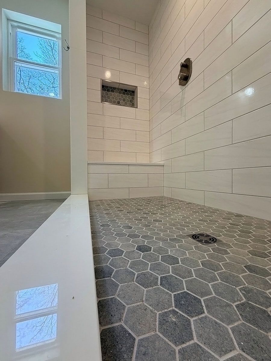 Empty tiled bathroom with hexagonal shower floor, white subway walls, and a frosted window.