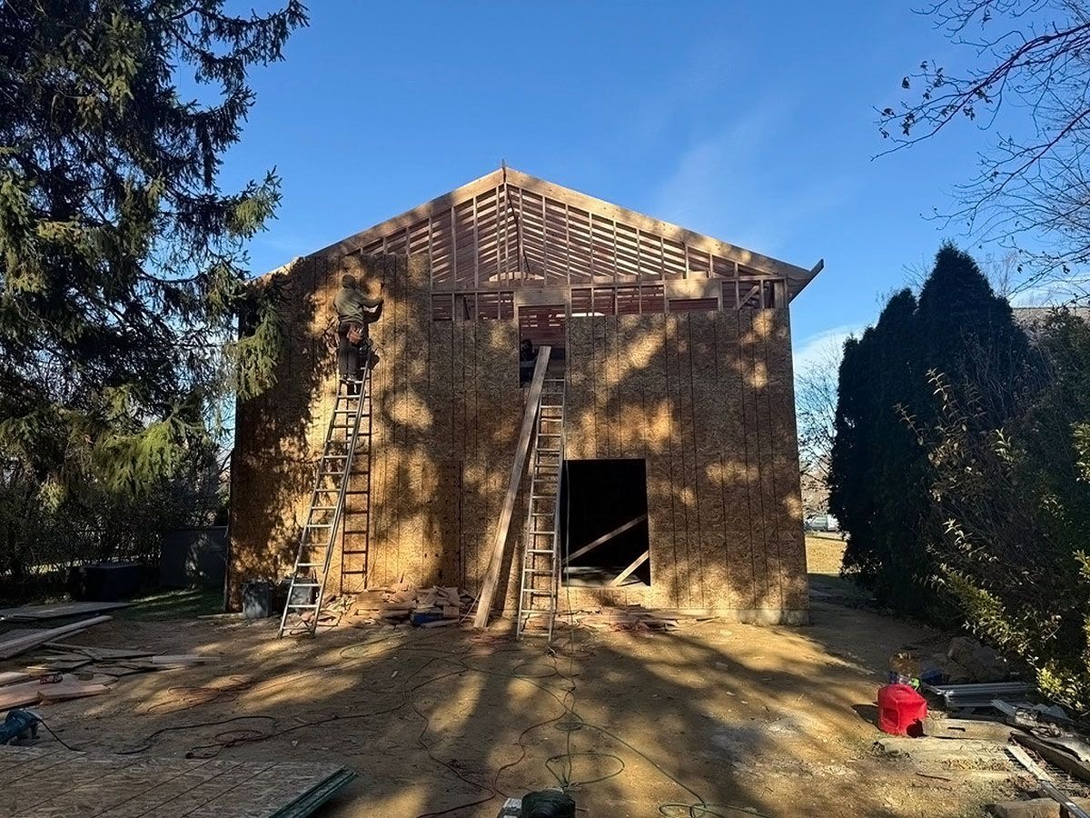 Partially built wooden house under construction on a sunny day, with trees and a clear blue sky.