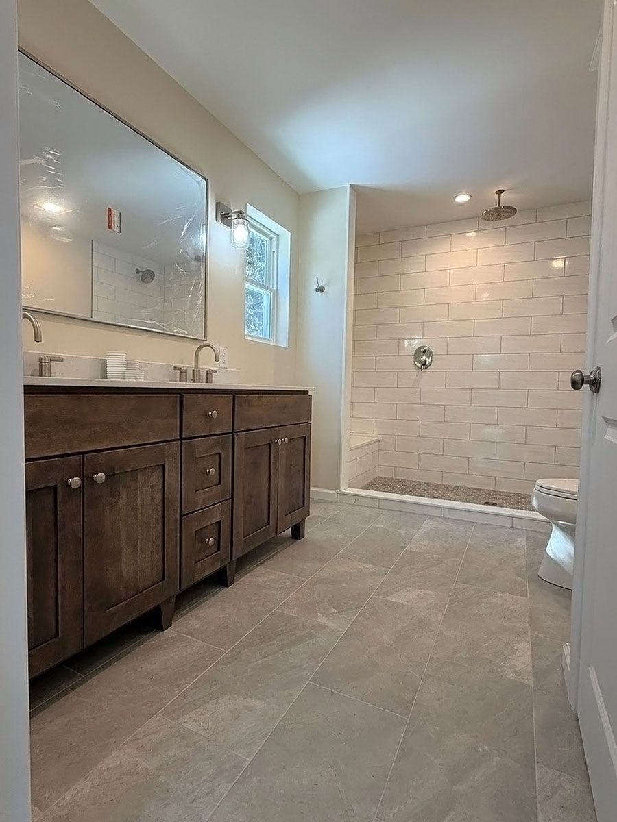 Spacious bathroom with dark wood vanity, large mirror, and tiled shower area.