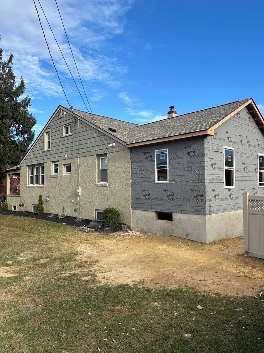 Gray stone house with sloped roof and small windows, viewed from a grassy yard under a blue sky