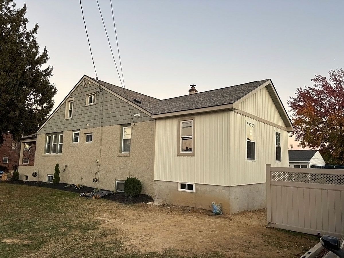 Suburban house with beige siding, gray roof, and a fenced yard under a clear sky