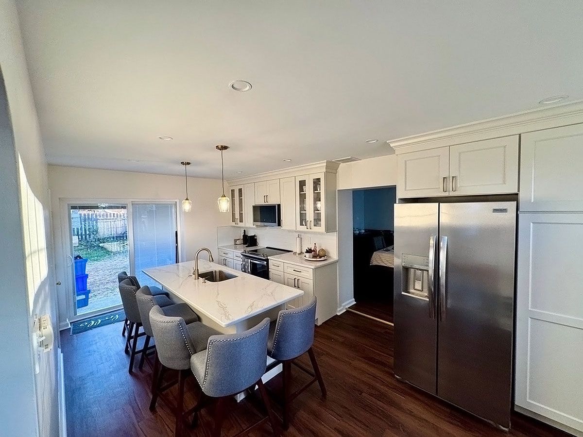 Bright kitchen with white cabinets, stainless steel fridge, island table, and chairs near a sunlit doorway