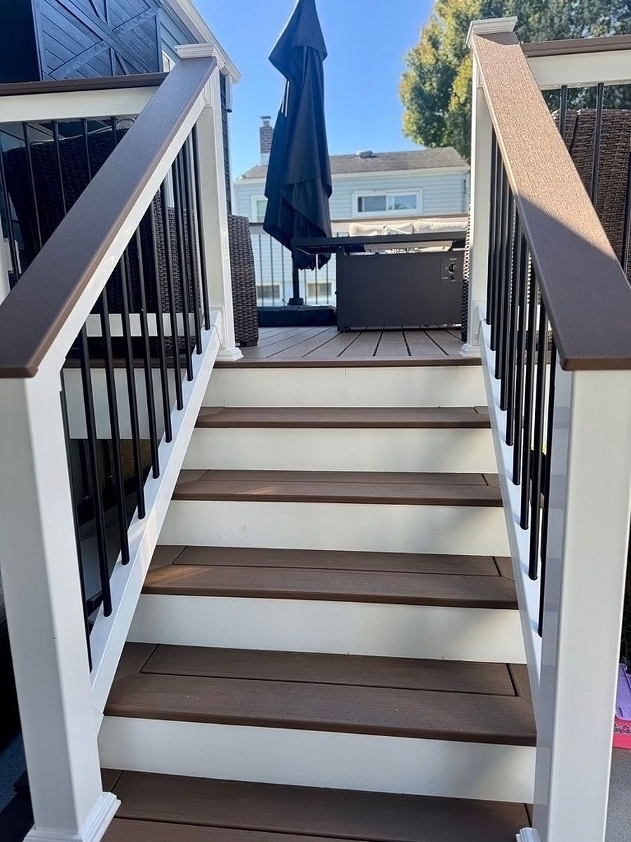 Outdoor staircase with white railings, black balusters, and a closed blue patio umbrella at the top.