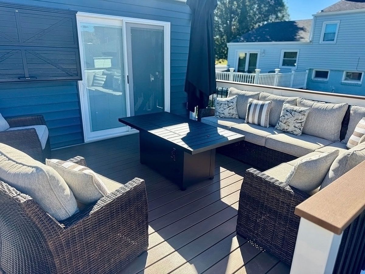 Outdoor patio with wicker seating, black coffee table, and cushioned sectional by a house deck