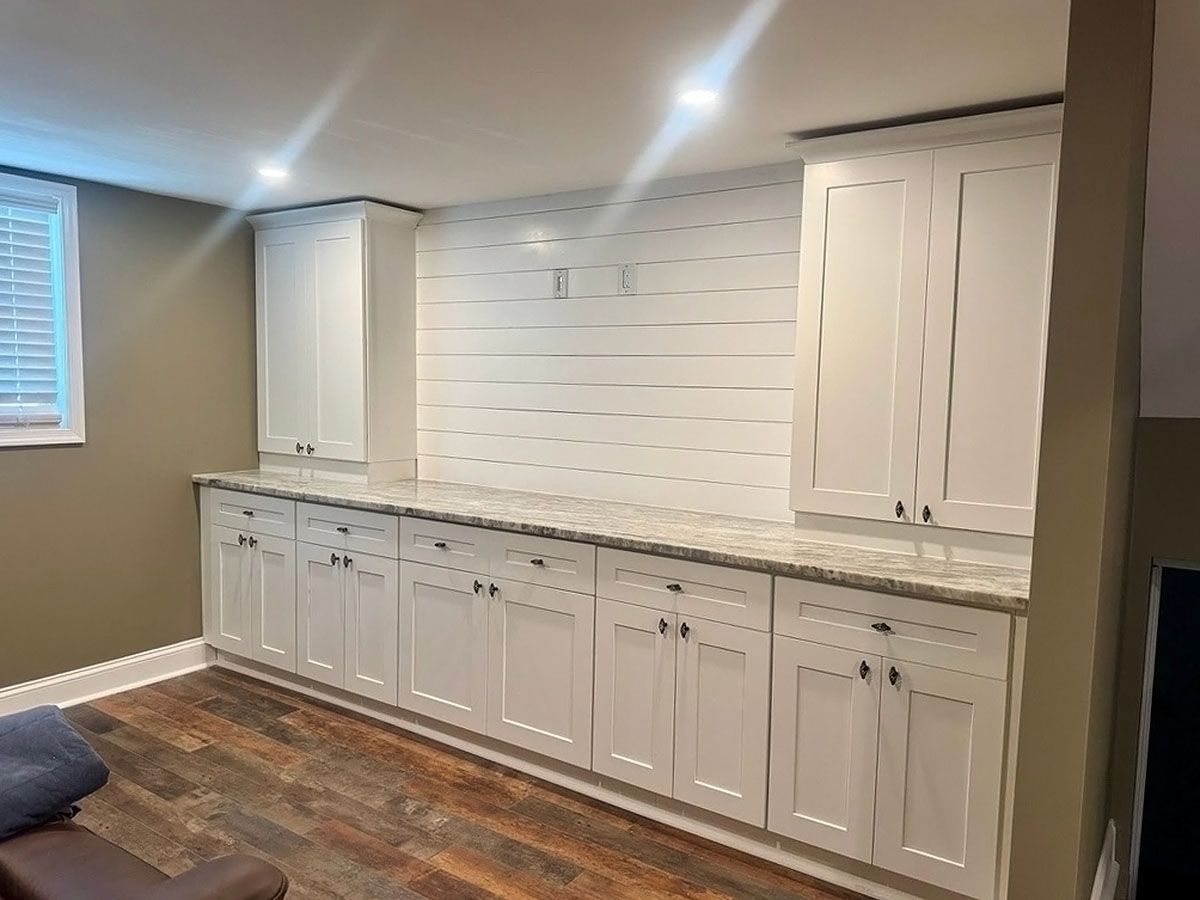 Built-in white cabinets and stone countertop along a wall in a finished basement room