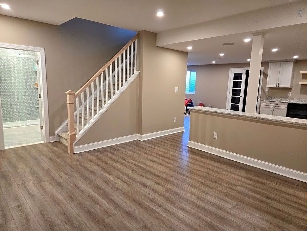 Empty living room with wood flooring, staircase, and open view into a kitchen area