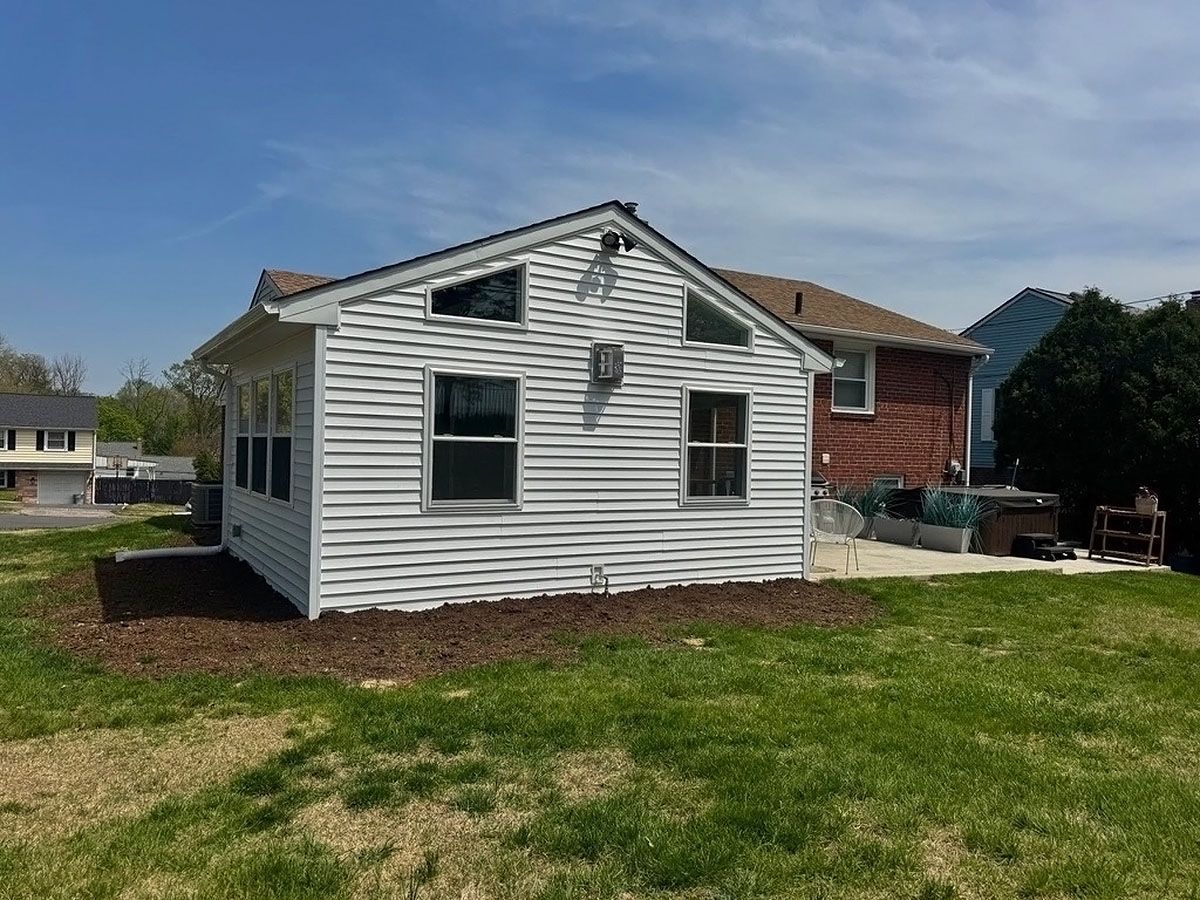 White-sided house exterior with dark shutters, red brick side, and a grassy yard under a blue sky