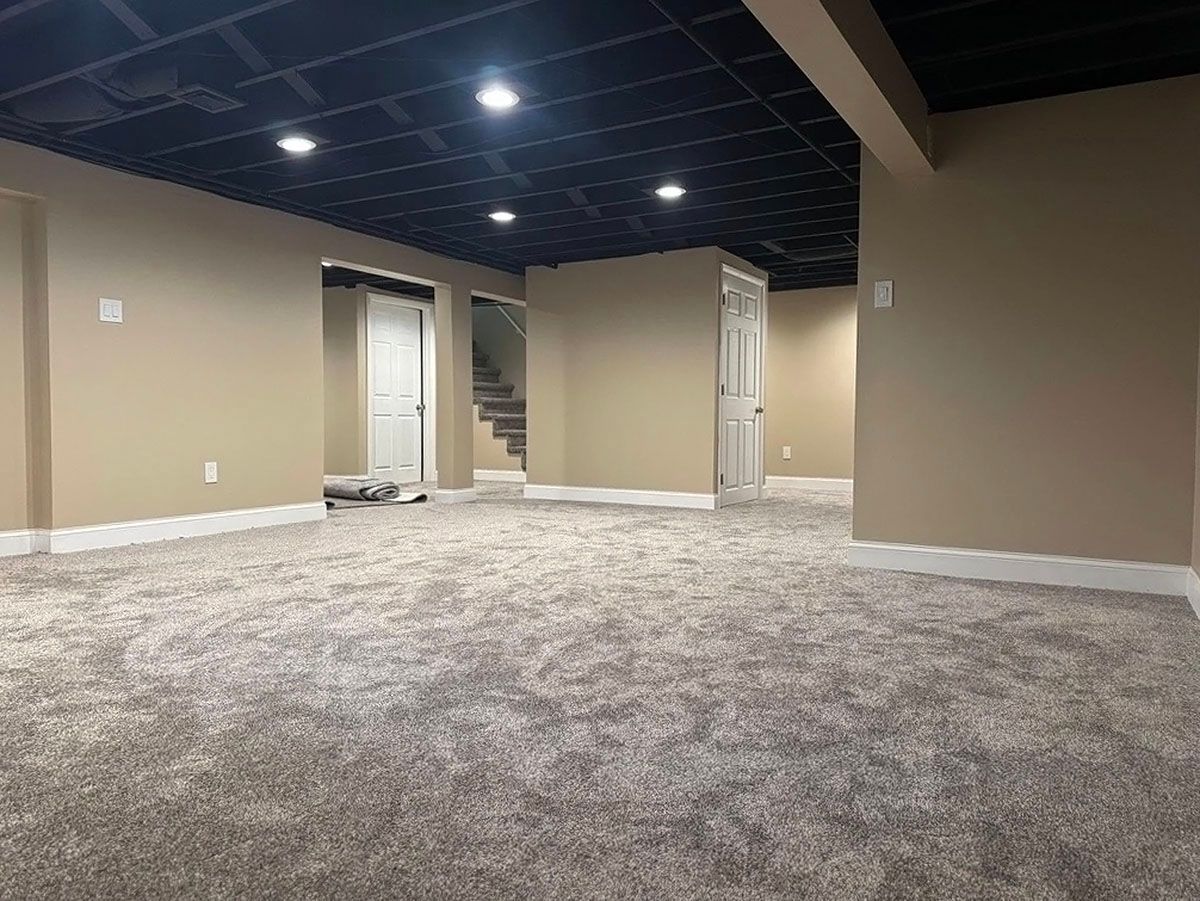 Empty carpeted basement room with beige walls, dark ceiling, and recessed lighting