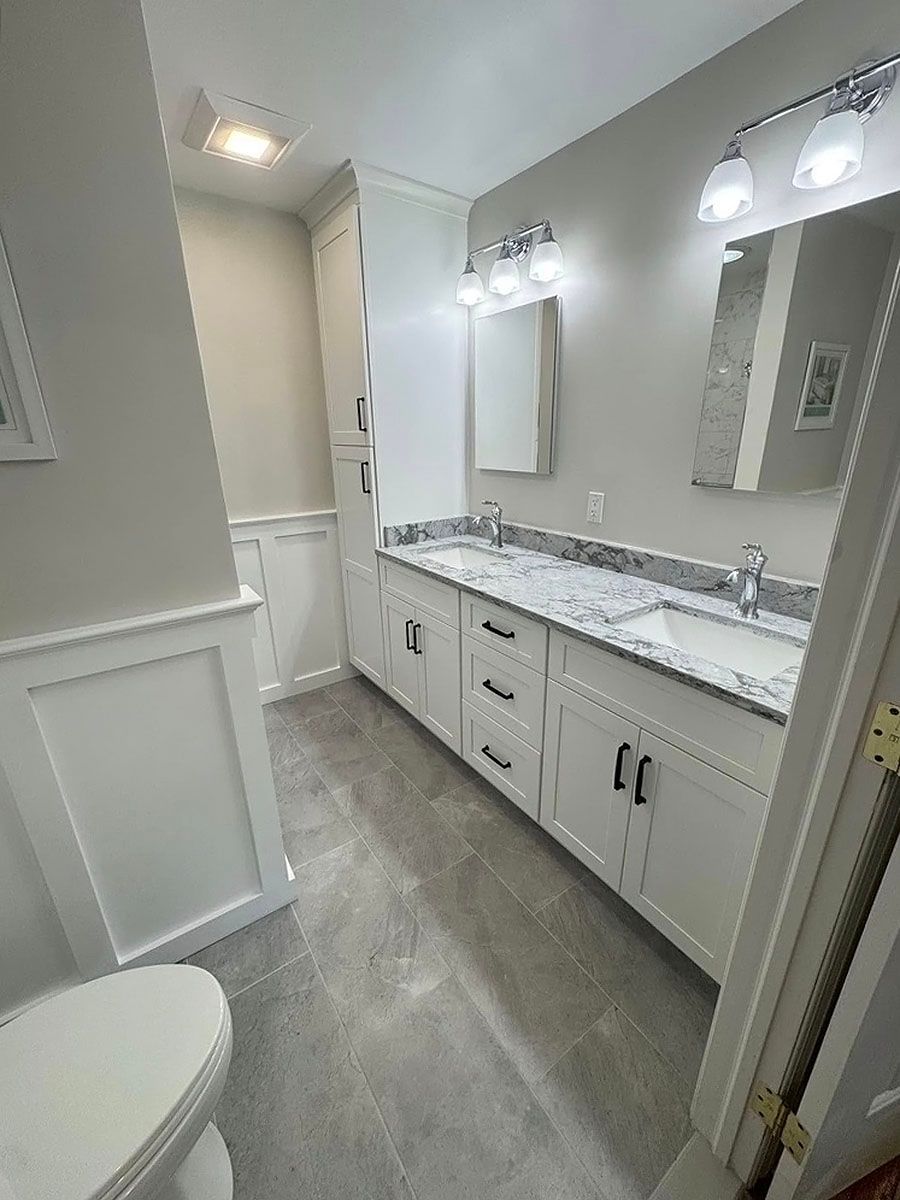Bright modern bathroom with double vanity, marble countertop, mirrors, and wall sconces