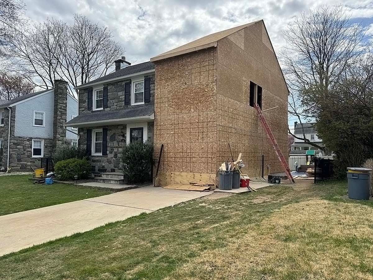 House under renovation with plywood-covered side wall, driveway, and lawn