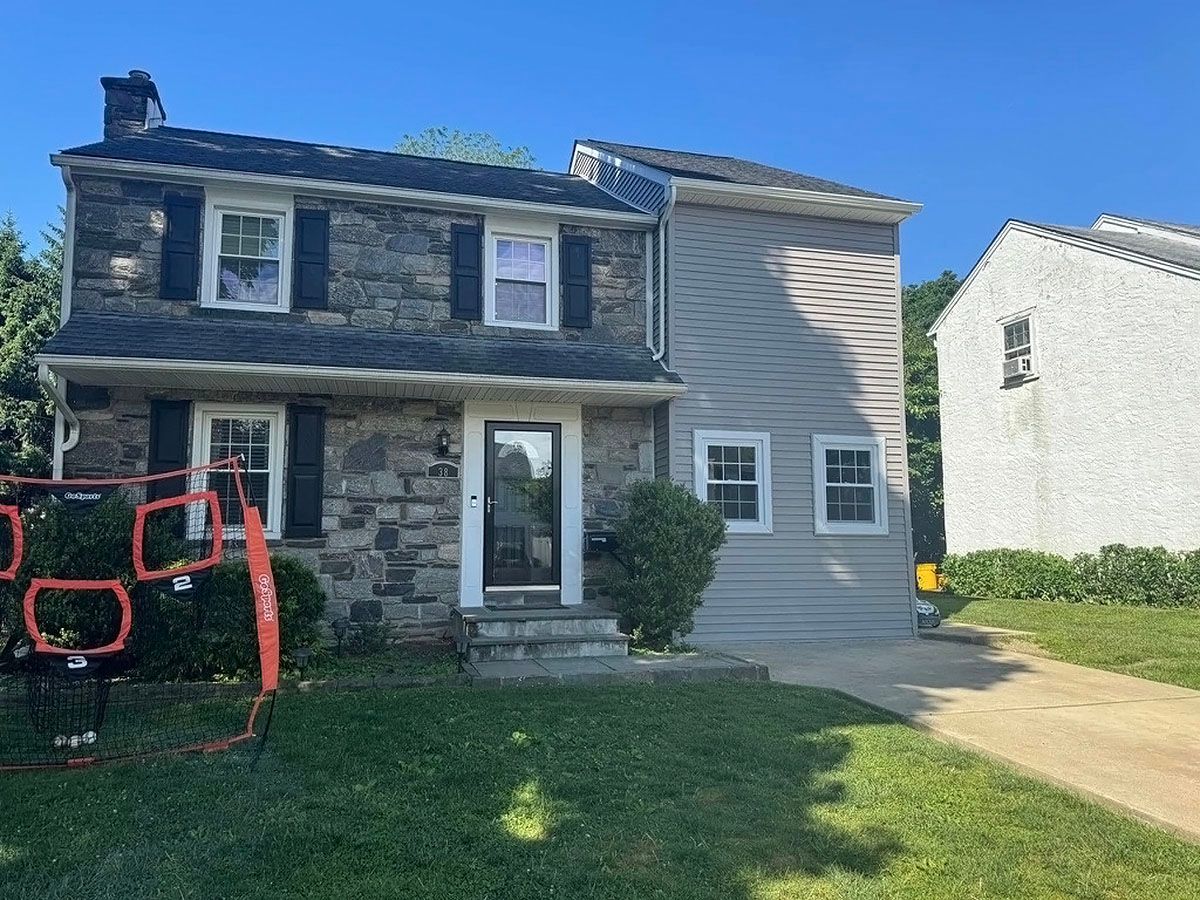 Two-story house with stone facade, white entry door, lawn, and driveway in front of neighboring homes