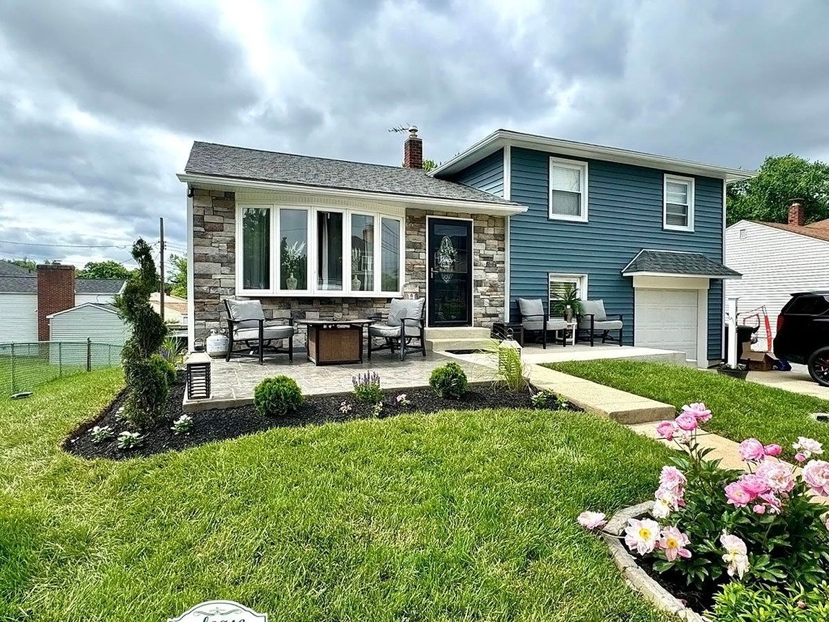 Blue-and-stone house with flowered front yard and walkway under cloudy sky