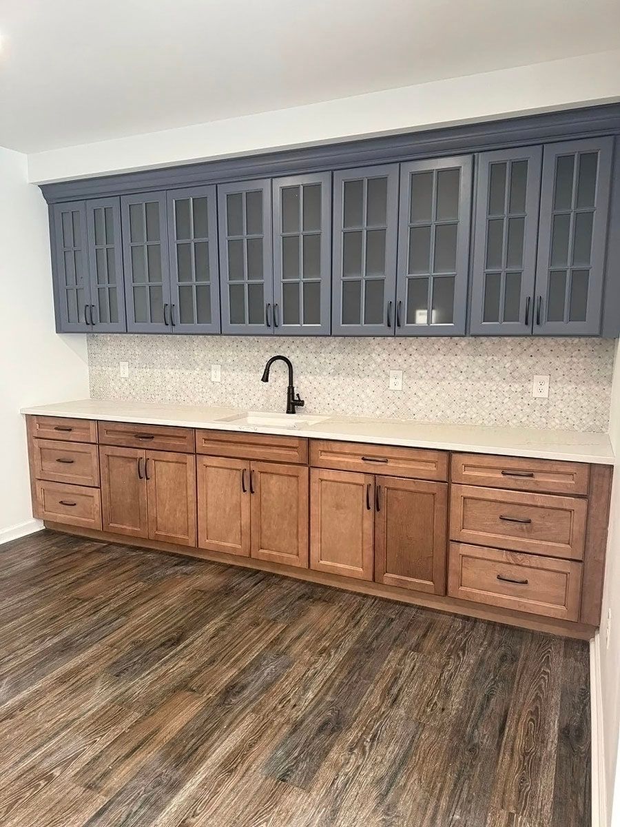 Modern kitchen with blue upper cabinets, wood lower cabinets, white backsplash, and dark wood floor