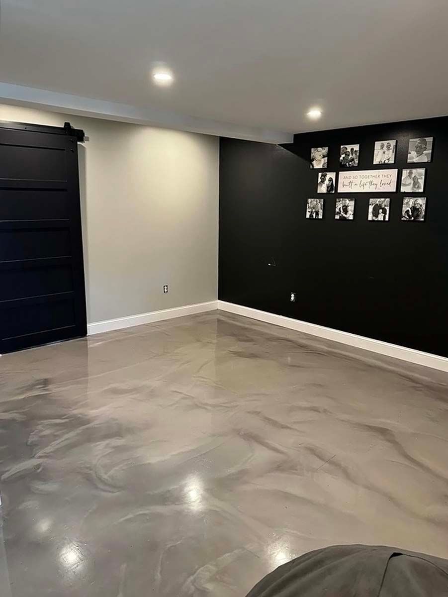 Empty modern room with black accent wall, glossy gray floor, and small wall art display