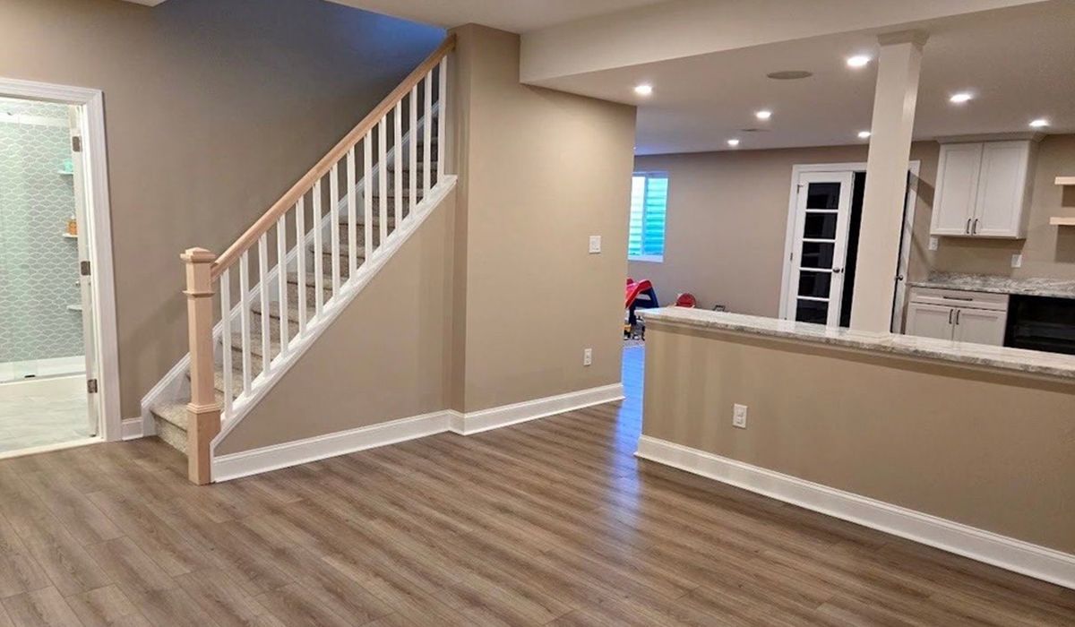 Empty modern living room with wood floors, staircase, and open kitchen area.