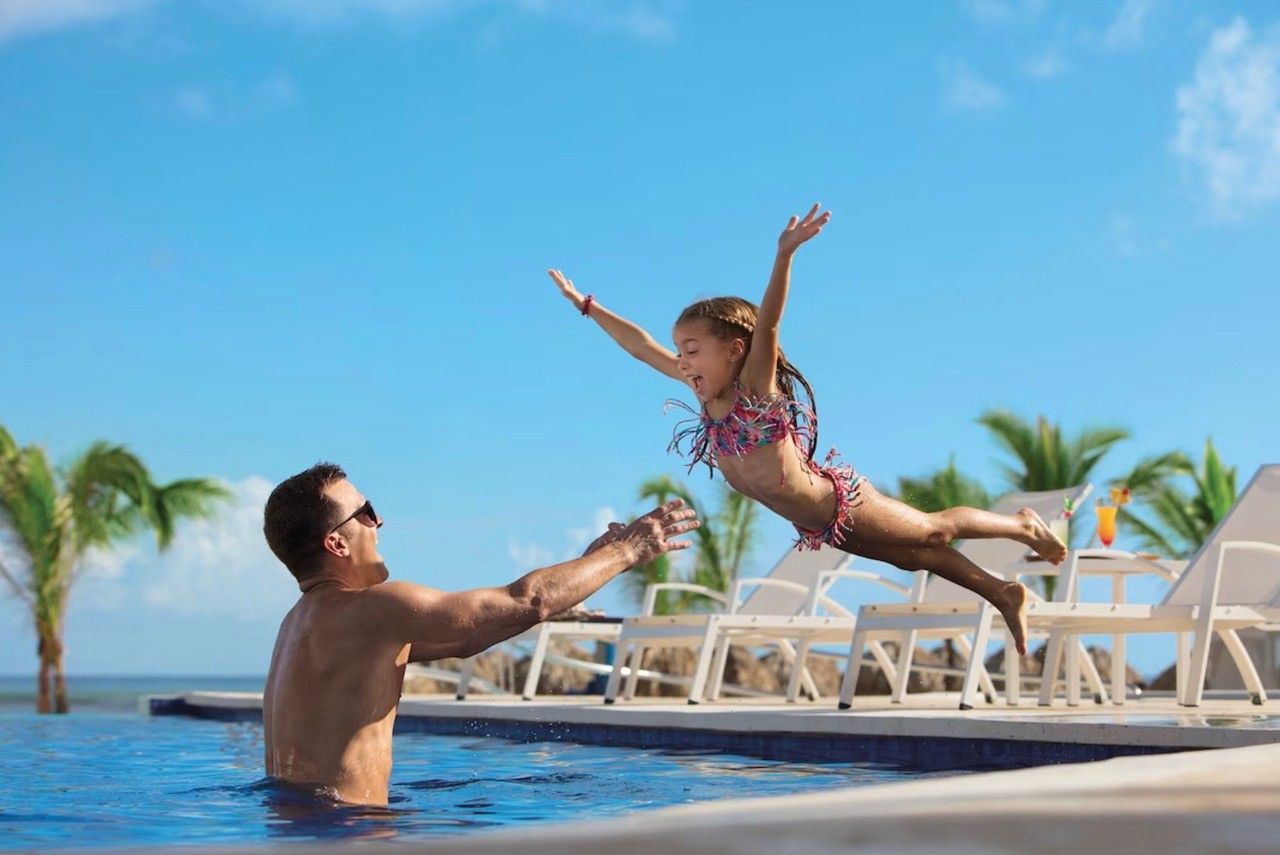 A man is holding a little girl in the air in a swimming pool.