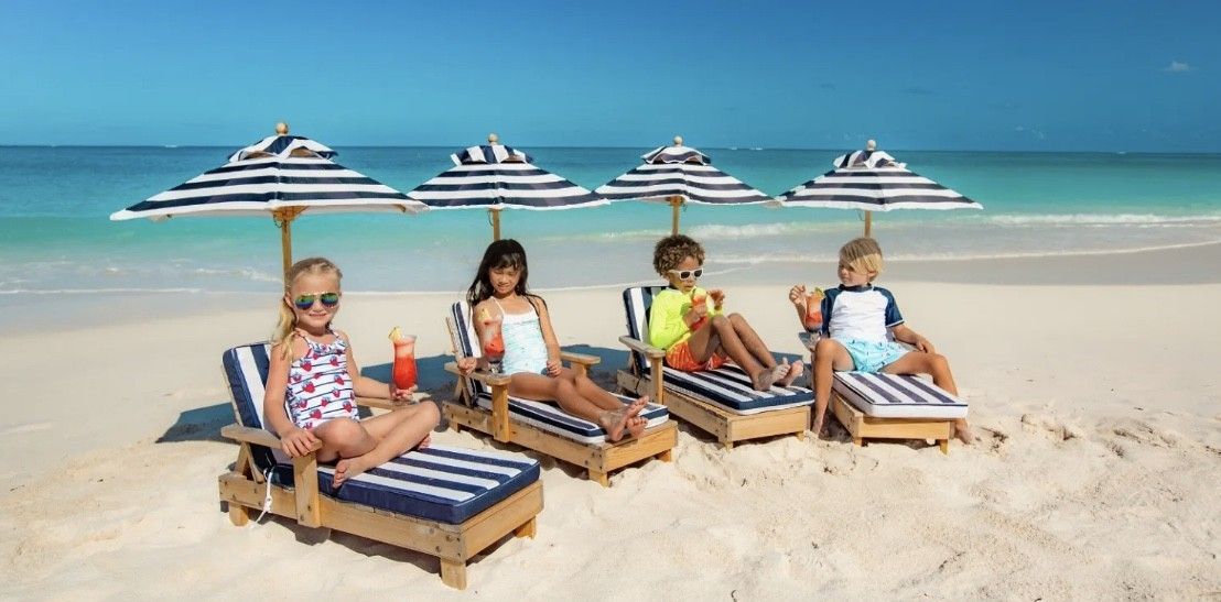 A group of children are sitting on the beach under umbrellas.