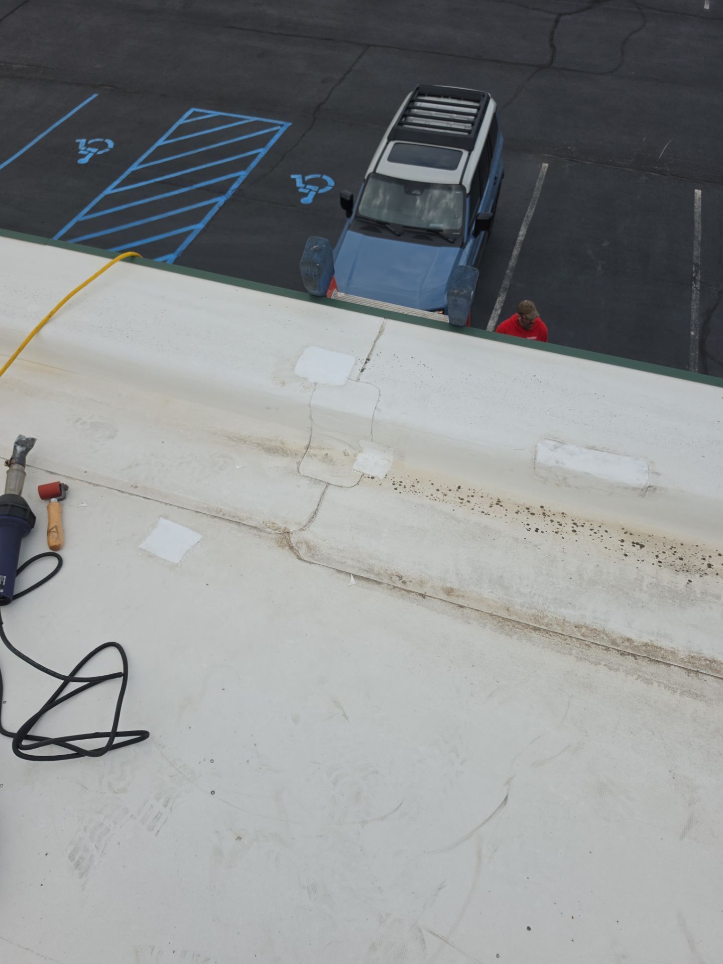 A view from a roof looking down at a parking lot with a blue vehicle parked in an accessible space.