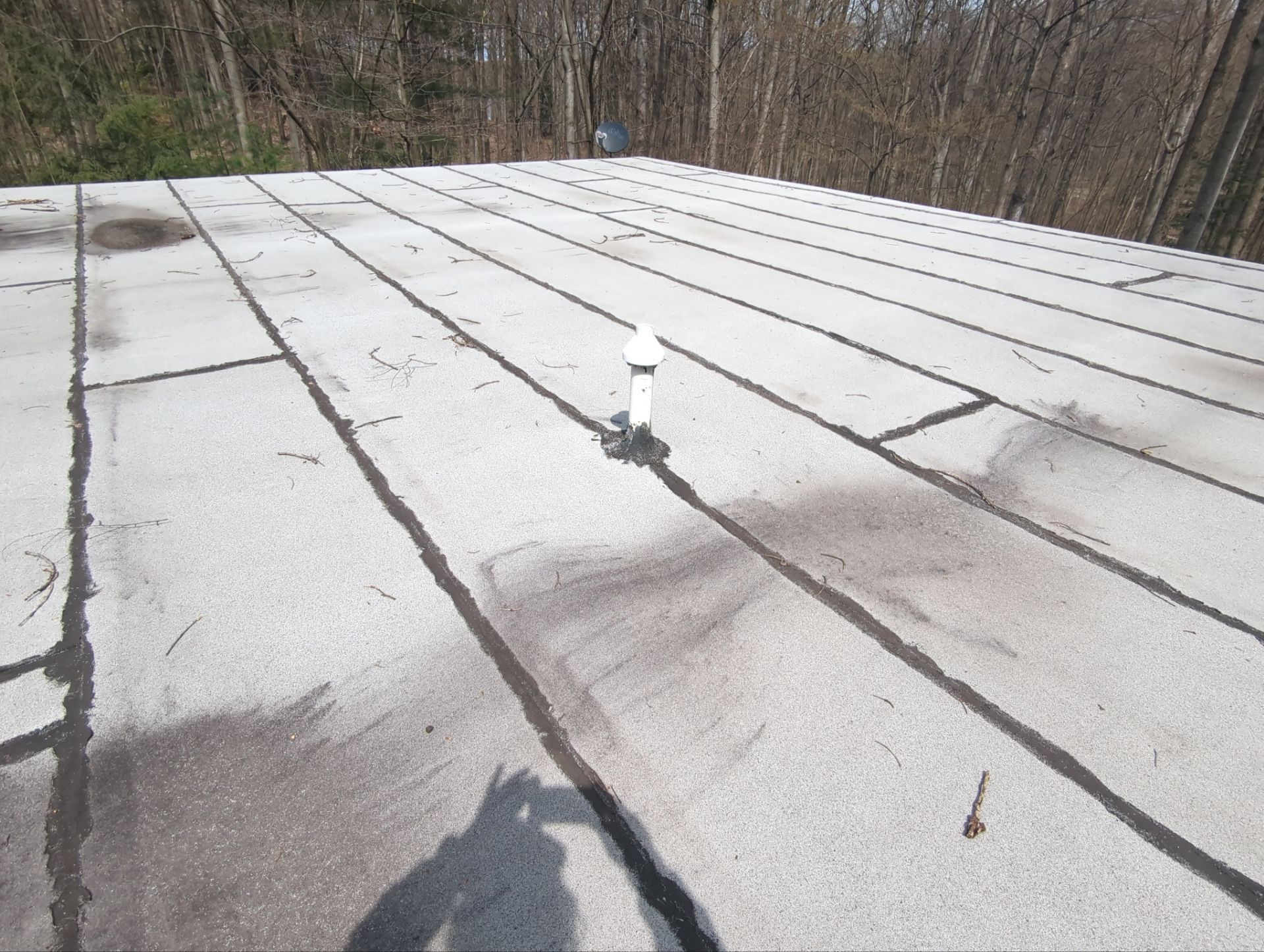 A flat, light gray roof surface featuring dark, taped seams and a white vent pipe protruding from the center.