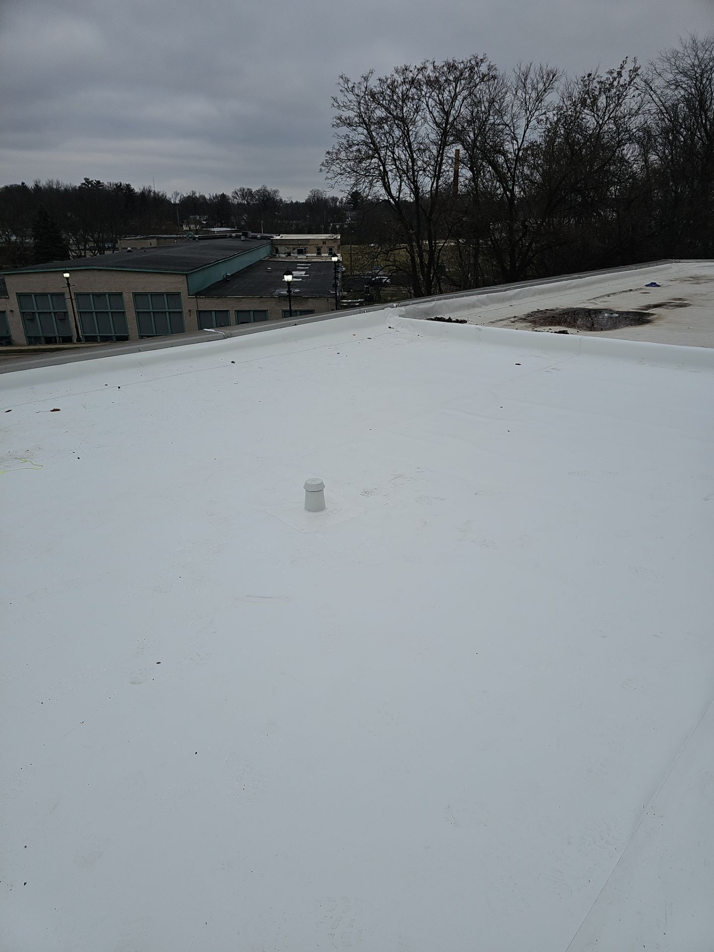 A flat, white-coated commercial roof under a cloudy sky, with a small vent pipe and a distant building in the background.
