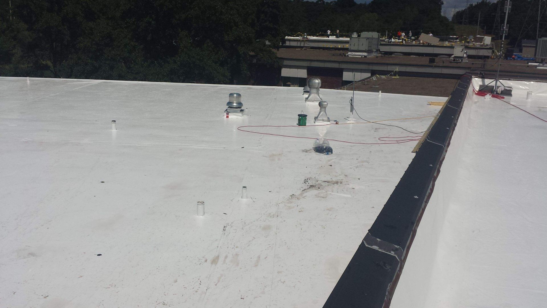 White flat roof featuring several metal ventilation pipes and drainage points, with a dark edge along the perimeter.