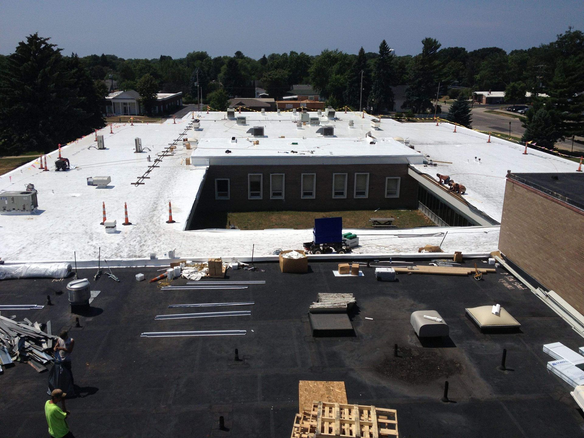 Aerial view of a flat commercial roof showing a white section under construction and a black section with supplies.