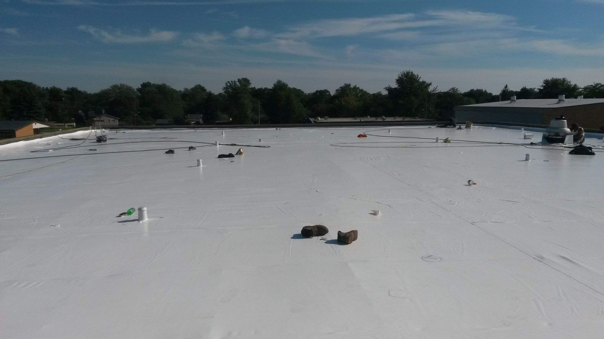 An elevated view of a flat, white commercial roof under a blue sky, with scattered debris and ventilation pipes.