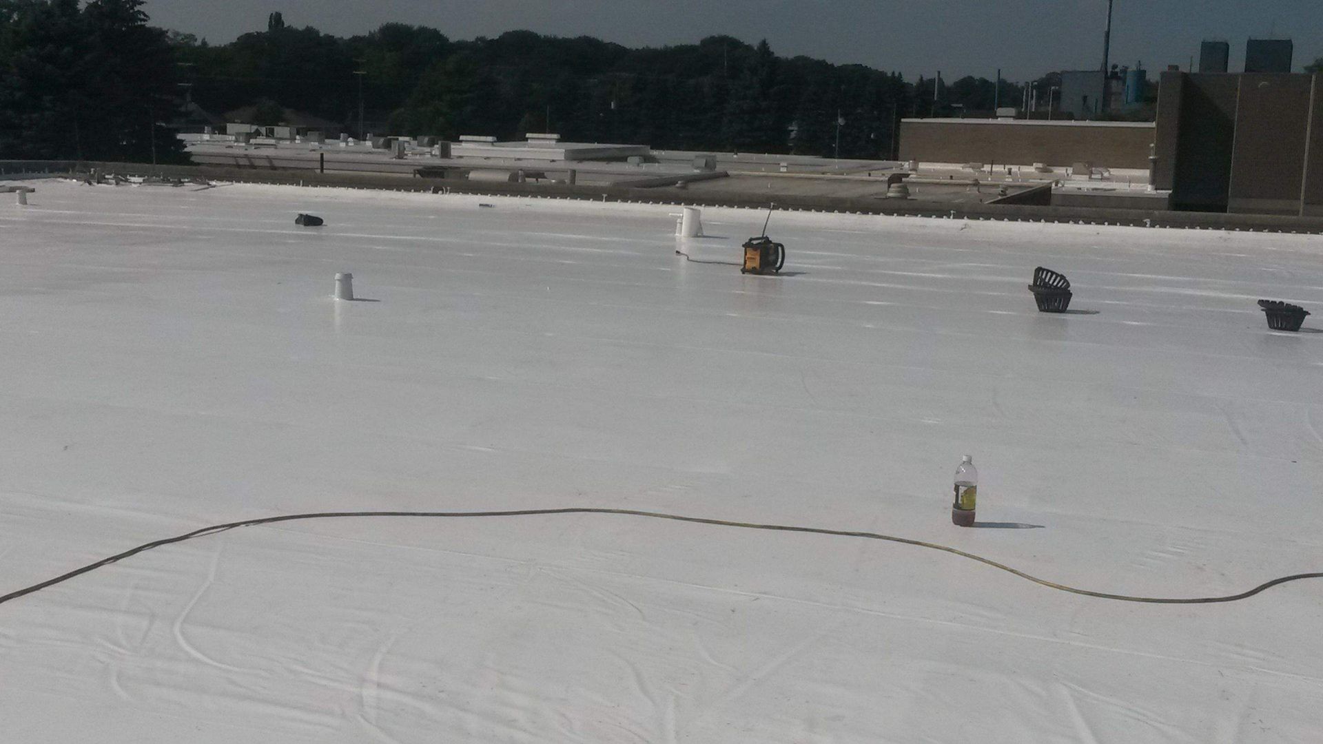 A worker uses a heat welder on a white, newly installed flat roof surface.