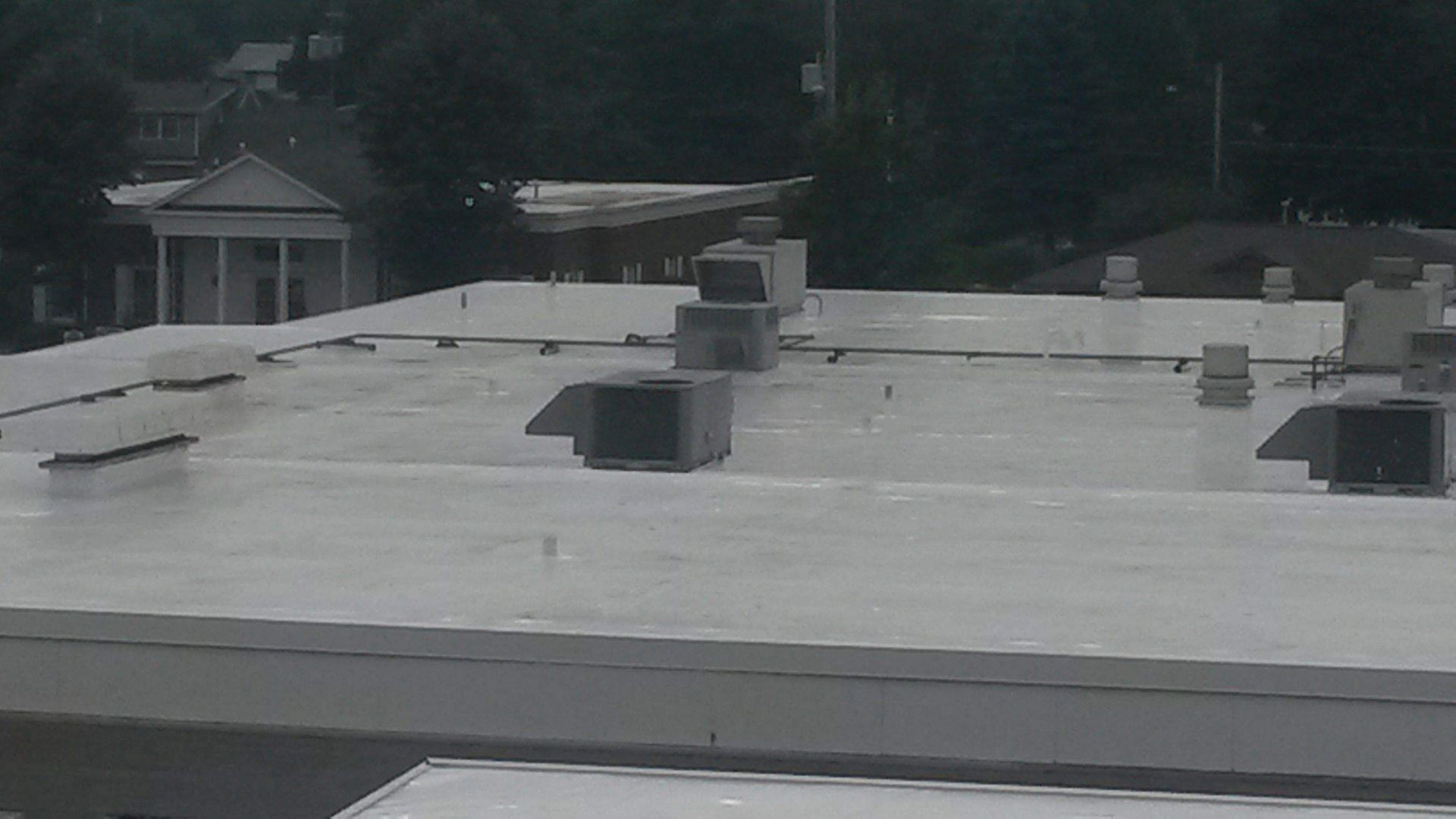 A flat, white commercial roof with several rectangular HVAC units, viewed from an elevated position.