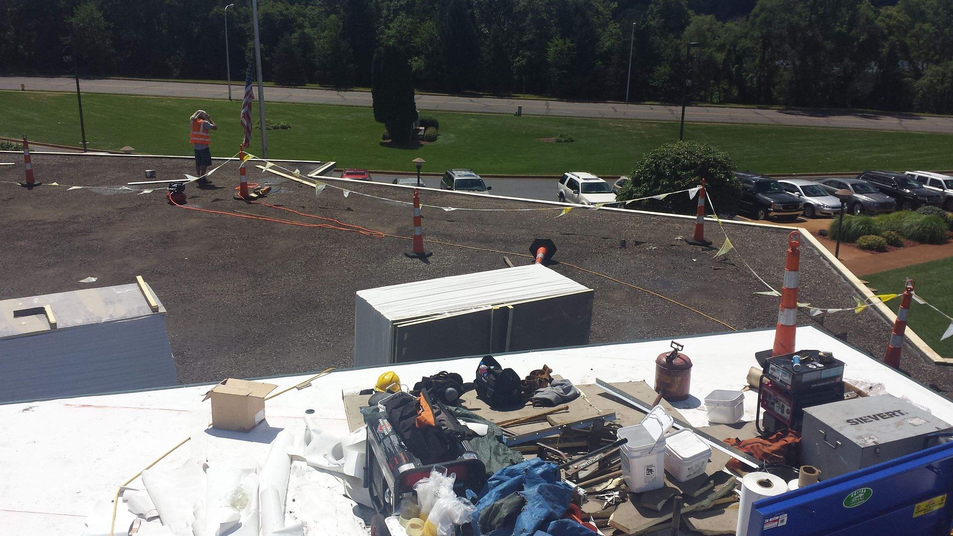 A rooftop construction site with a worker, gravel roof sections, and equipment on a white membrane surface.