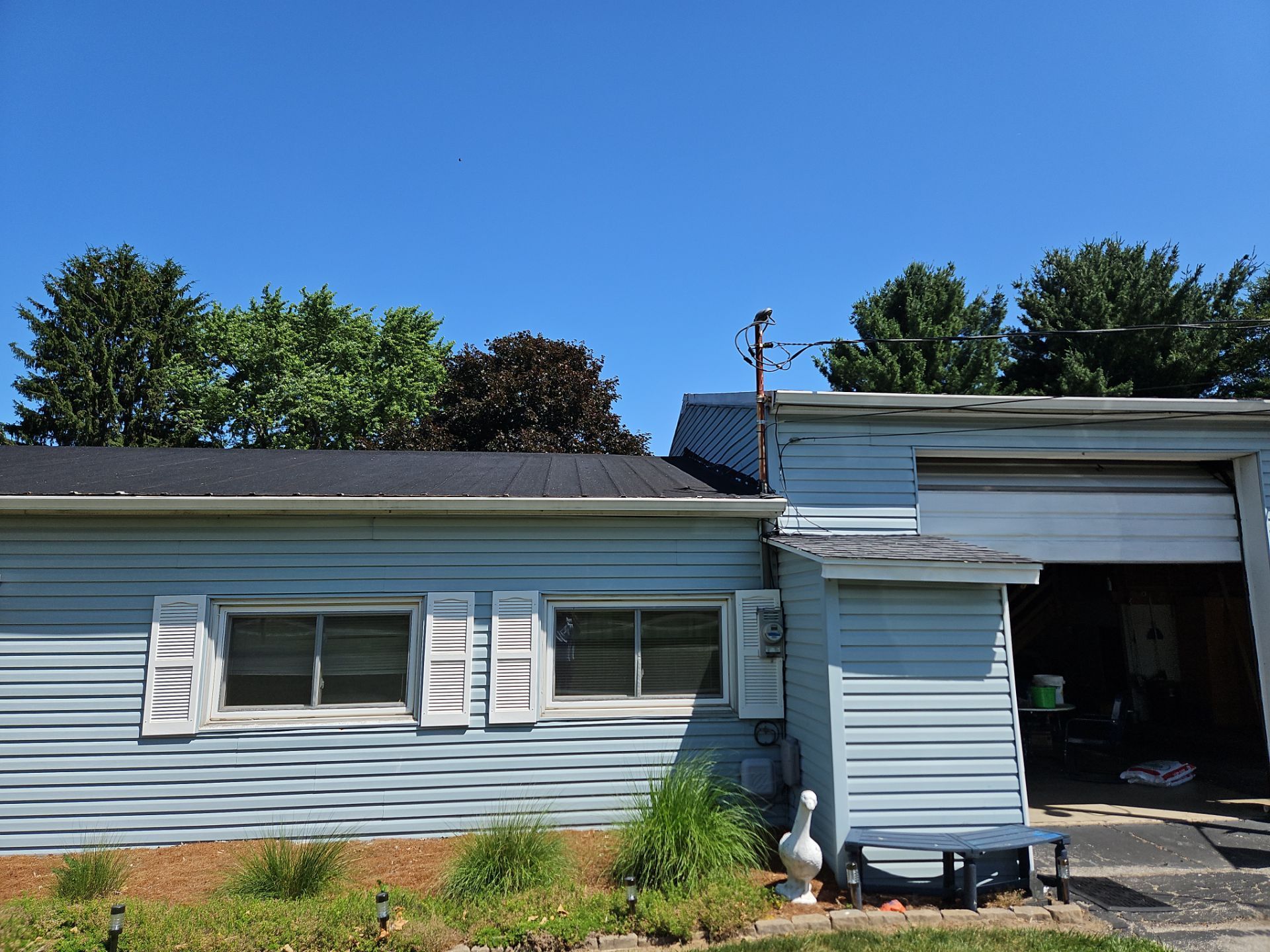 A light blue, one-story building with white shutters, a dark roof, and a garage entrance, set under a clear blue sky.