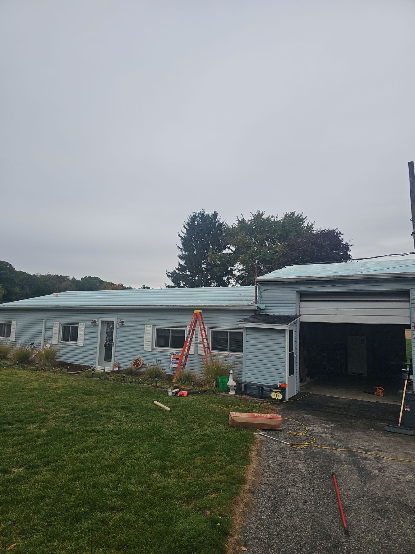 A light blue, single-story house with a garage and a ladder leaning against the front during exterior construction.