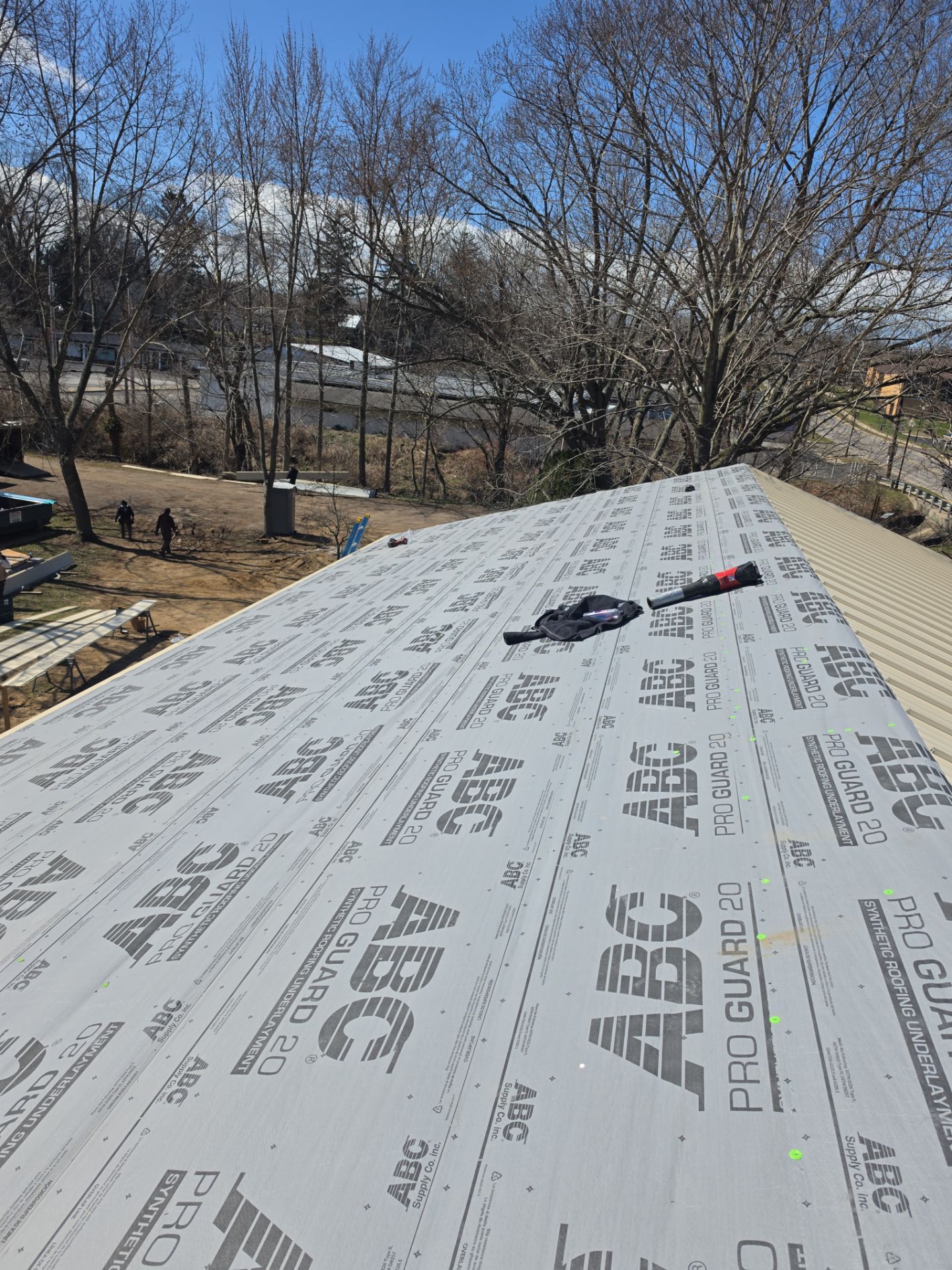 A partially roofed structure covered in gray, branded underlayment, with a nail gun lying on the surface.