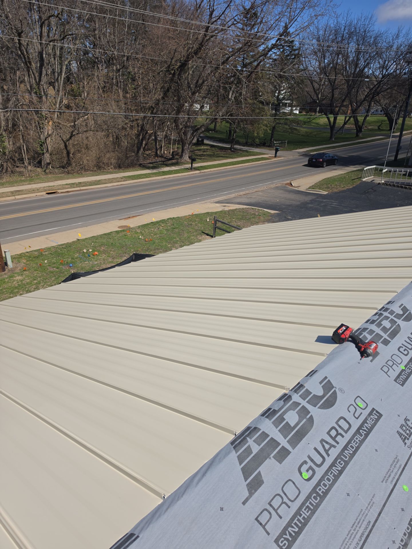 A high-angle view of a beige metal roof under construction with a roll of ABC Pro Guard 20 underlayment in the foreground.