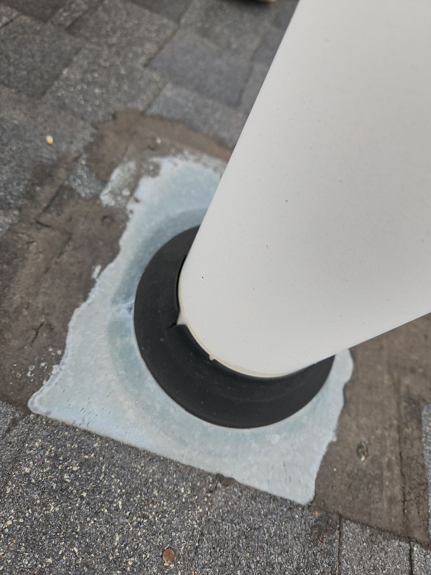 A white post secured to a paved surface with a black circular seal and grey sealant surrounding the base.