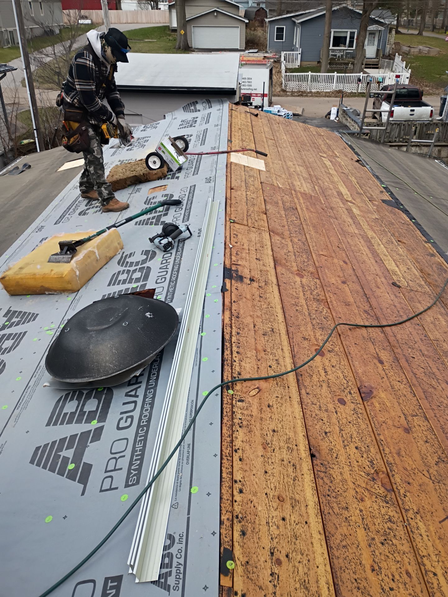 A worker installs underlayment on a roof with exposed wooden decking and a metal edge strip.